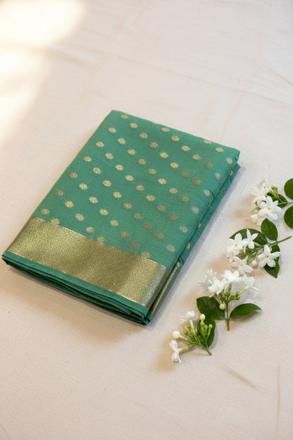 Green saree with gold patterns on a light wooden surface