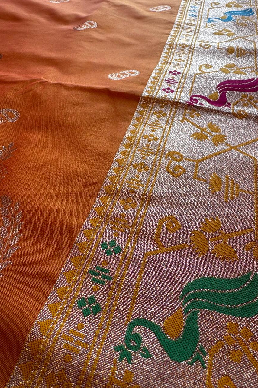 Close-up of a traditional embroidered fabric with intricate patterns on an orange and pink background.